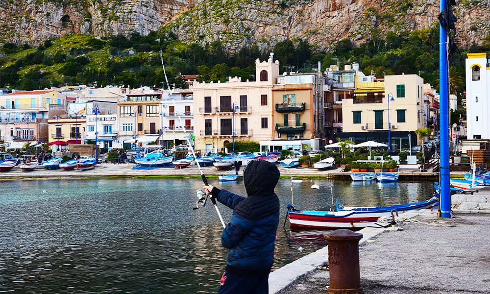 Menino pescando na praia siciliana de Mondello 